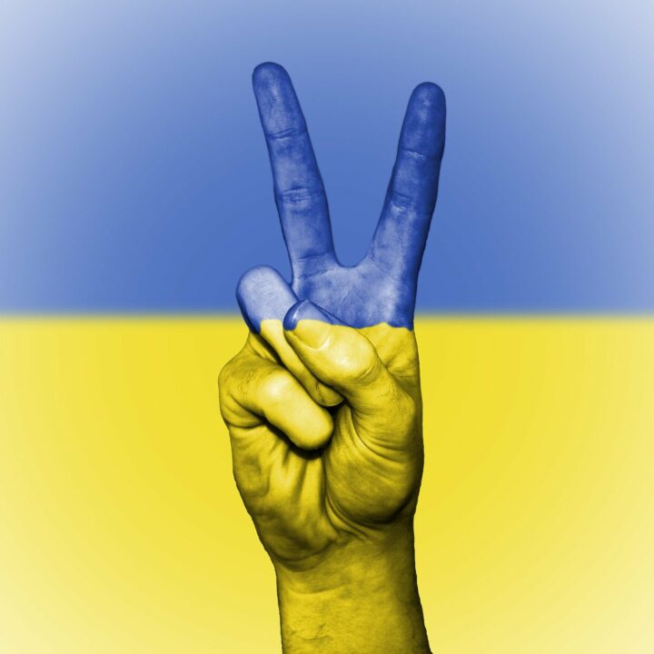 Hand mit Peace-Zeichen vor der ukrainischen Fahne.