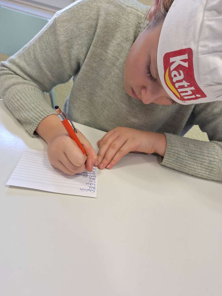 Ein Kind mit einer Kochmütze schreibt ein Rezept auf.