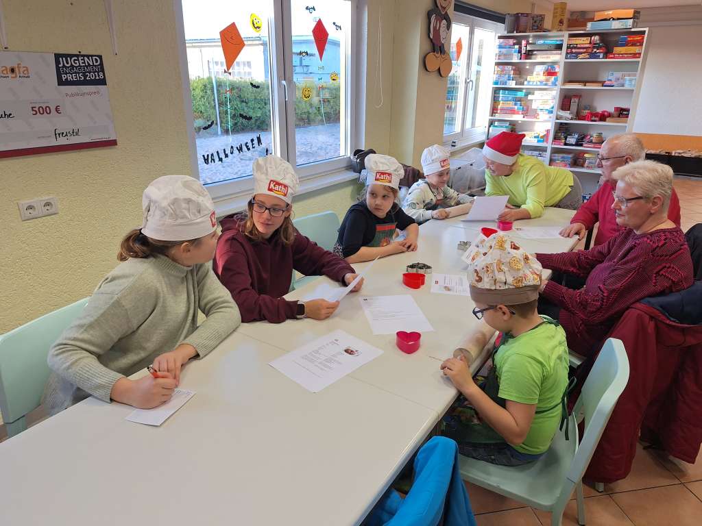 An einem Tisch sprechen verschiedene Kinder und Erwachsene über unterschiedliche Rezepte. Die Stimmung ist fröhlich und entspannt.