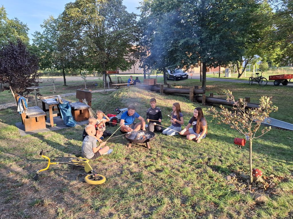 Kinder sitzen um eine Feuerschale und grillen Mashmallows